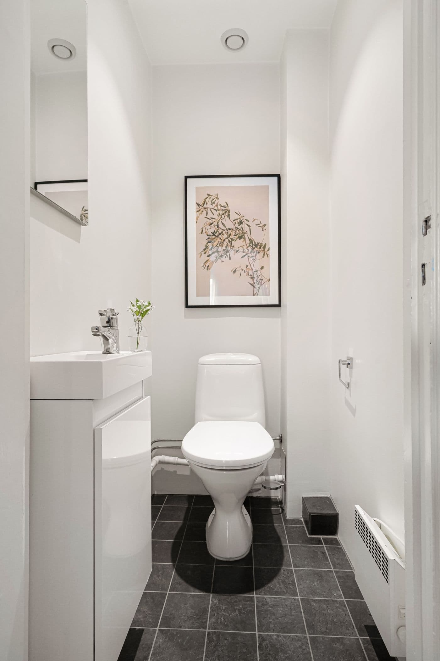 Lyst badeværelse med hvidt toilet og håndvask, indrammet plakat på væggen